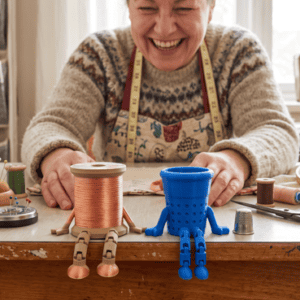 Colorful 3D printed robot figures on a craft table with a smiling woman. Acadiana3DPrints